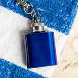Blue 1oz clip on keychain flask lying on a striped beach towel, a bachelor party gift idea