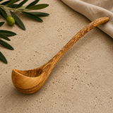 Long olive wood soup ladle with a deep bowl and swirling grain on a linen cloth