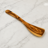 Plain olive wood spatula lying on marble, a handmade wooden cooking utensil
