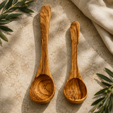 Set of two olive wood cooking ladles in large and small sizes on linen with olive branches