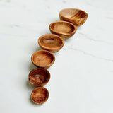 Six olive wood nesting bowls lined up from smallest to largest on white marble