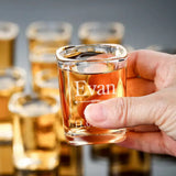 Custom 2.2 oz shot glass engraved with a sample name held up in front of more shot glasses