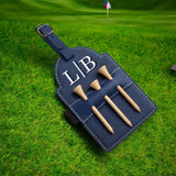 Navy leather golf tee holder with sample initials and wood tees lying on a golf green