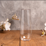 Plain clear plastic champagne flute on a wood table with white flowers, sold single or in bulk sets