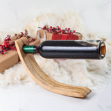 Side view of a handmade olive wood wine bottle holder balancing a bottle horizontally among holiday gifts