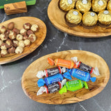 Three oval olive wood serving trays holding nuts, chocolates and candy, a snack serving set