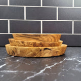 Side view of the stacked olive wood serving trays showing their shallow curved shape