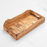 Empty rustic olive wood serving tray with cutout handles and live edge sides on a white surface