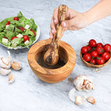 Hand grinding pepper with an olive wood pestle in a matching handmade mortar on a marble counter