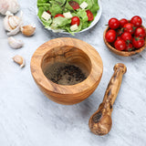 Olive wood mortar filled with ground pepper with the pestle lying beside it on a marble counter