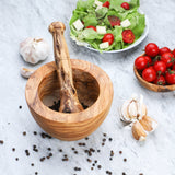 Handmade olive wood mortar and pestle surrounded by garlic, tomatoes, salad and scattered peppercorns