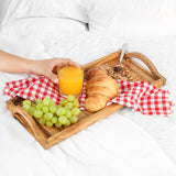 Hand reaching for orange juice on an olive wood breakfast tray with grapes and a croissant