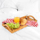 Olive wood tea and vanity tray with orange juice, grapes and a croissant on a red checked napkin