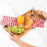 Hands carrying an olive wood serving tray with orange juice, grapes and a croissant