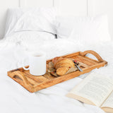 Olive wood breakfast tray with handles holding a coffee mug and croissant on white bedding