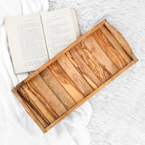 Empty handmade olive wood serving tray with handles showing striped natural grain beside a book
