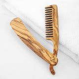 Handmade olive wood beard comb half open on a white towel showing the pivot and natural grain