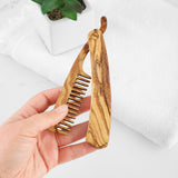 Hand holding a closed olive wood folding beard comb with the teeth tucked into the handle