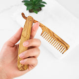 Hand holding a handmade olive wood folding beard comb opened to show the wide teeth and grain