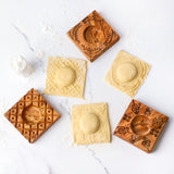 Olive wood Italian pasta molds surrounded by finished square ravioli on a floured white surface
