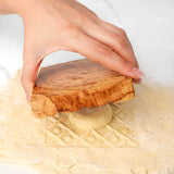 Hand pressing an olive wood ravioli mold into pasta dough to stamp a filled ravioli