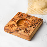 Olive wood pasta mold with carved fleur pattern and round center cavity on a white surface