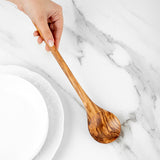 Hand holding an olive wood cooking spoon by the handle above white plates
