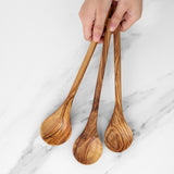 Hand holding three long handmade olive wood cooking spoons over white marble