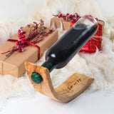 Olive wood wine bottle holder engraved with a sample name, balancing a wine bottle in a holiday gift scene