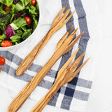 Olive wood salad forks on a blue striped kitchen towel next to a bowl of salad
