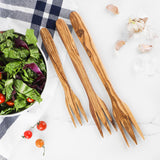 Three handmade olive wood salad and pasta forks laid beside a bowl of mixed greens and cherry tomatoes