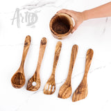 Five handmade olive wood utensils laid out with a hand holding the empty holder