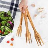 Hand holding three wooden forks for salad and pasta of different sizes beside a salad bowl