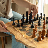 Player moving a black chess piece on a live edge olive wood chess table with dark squares