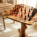 Olive wood chess table with red squares and a chess game set up beside a chair