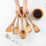 Hands holding five olive wood kitchen utensils fanned out beside the holder
