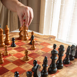 Close-up of a game in progress on an olive wood chess board with red and natural squares