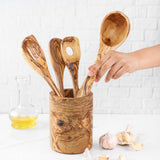Hand placing a spoon into an olive wood utensil holder next to olive oil and garlic