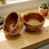 Two round olive wood bowls on a kitchen counter, one tipped to show the inside grain