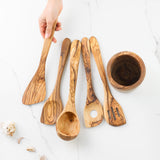 Hand arranging five olive wood utensils in a row next to the holder on marble