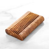 Empty olive wood soap dish with carved drainage grooves on white marble