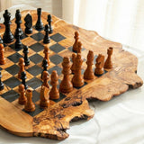 Close-up of black and natural wooden chess pieces on a handmade olive wood board