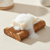 Olive wood soap saver tray holding a lathered bar of soap in a bright bathroom