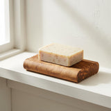 Olive wood soap dish with a bar of handmade soap on a white bathroom windowsill