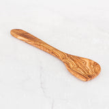 Single olive wood corner spoon with an angled flat edge lying on white marble