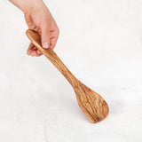 Hand holding a handmade olive wood corner spoon by the handle on white marble